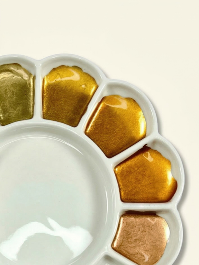 White paint palette with gold and bronze color swatches on a beige background
