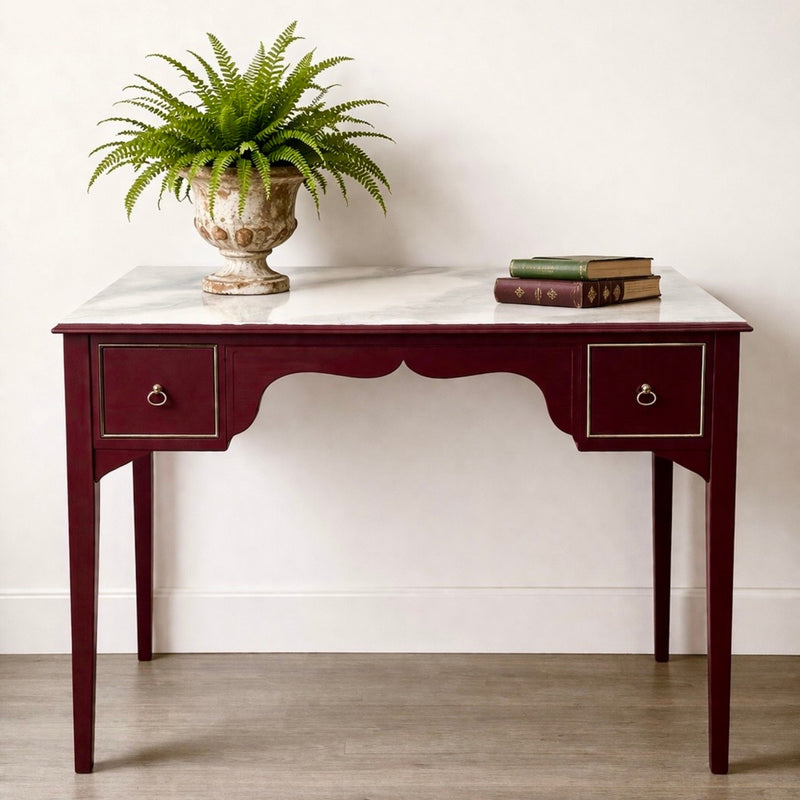 Murrey red dark burgundy painted wooden desk with marble table top. The desk has a plant and some books on top
