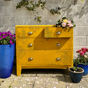 
                      
                        Oxford Ochre Yellow painted distressed dresser with floral arrangements against a stone wall.
                      
                    