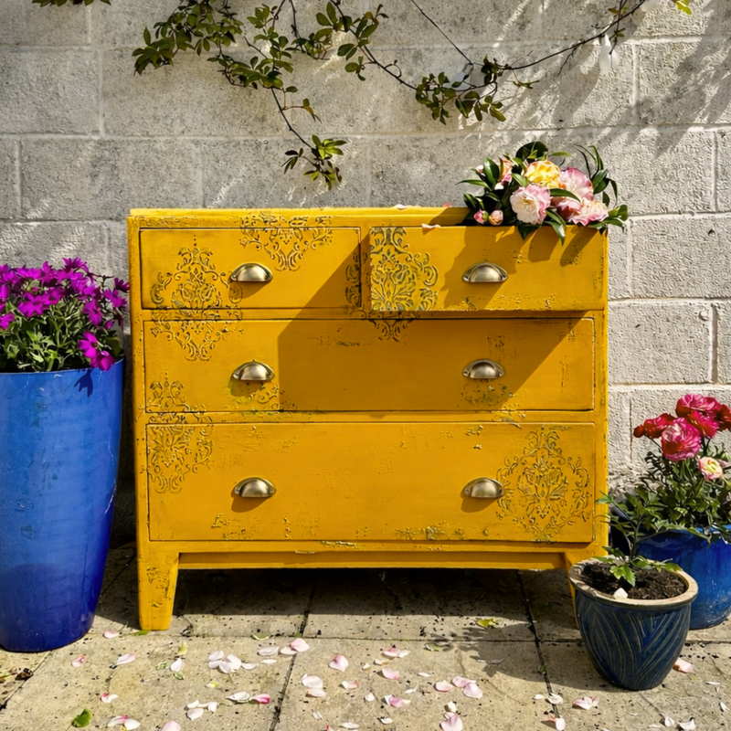 Oxford Ochre Yellow painted distressed dresser with floral arrangements against a stone wall.