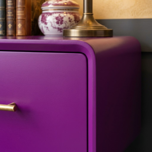 
                      
                        A close-up of a vibrant purple nightstand or cabinet with a gold drawer pull handle, styled with a brass lamp base and a decorative ceramic jar on top.
                      
                    