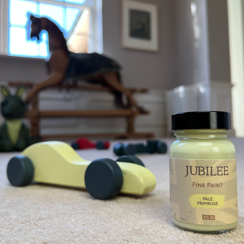 Bottle of Jubilee Fine Paint in Pale Primrose colour on a carpeted floor with toys in the background.