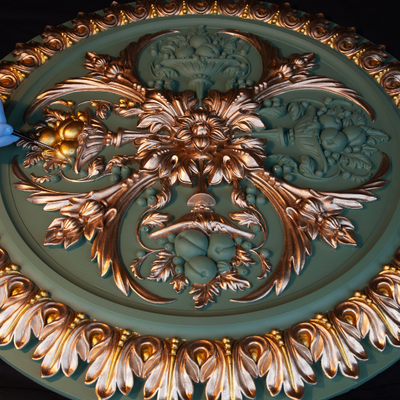 Decorative ceiling medallion with intricate gold and bronze designs on a green background