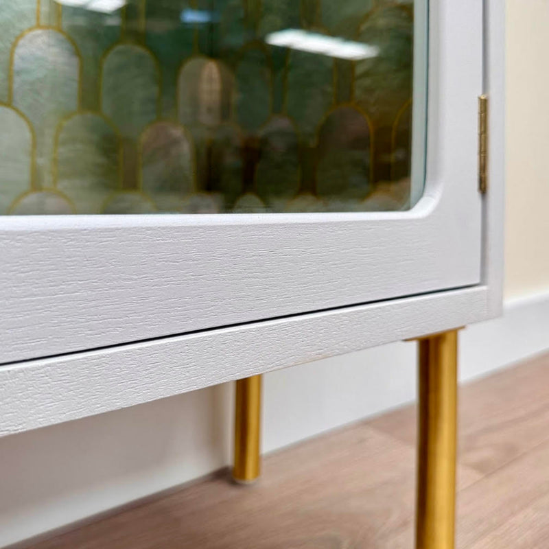 Close-up of a white cabinet with gold legs on a wooden floor.