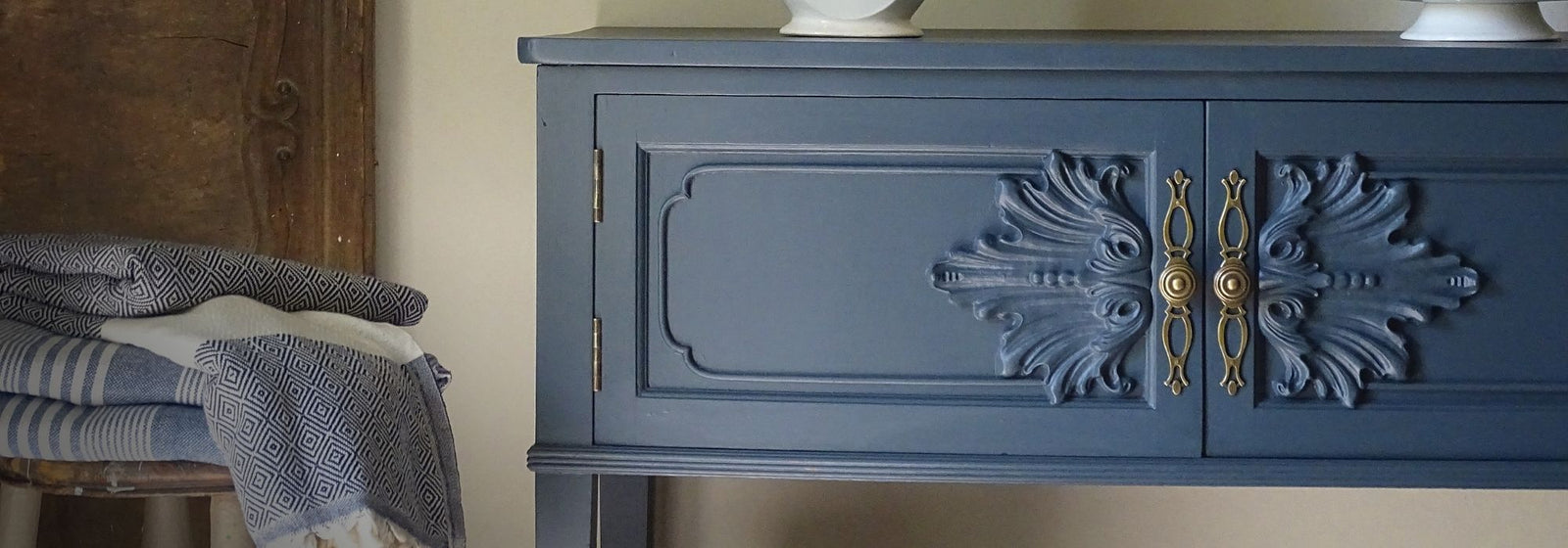Blue sideboard with decorative elements and folded clothes on a wooden stool.