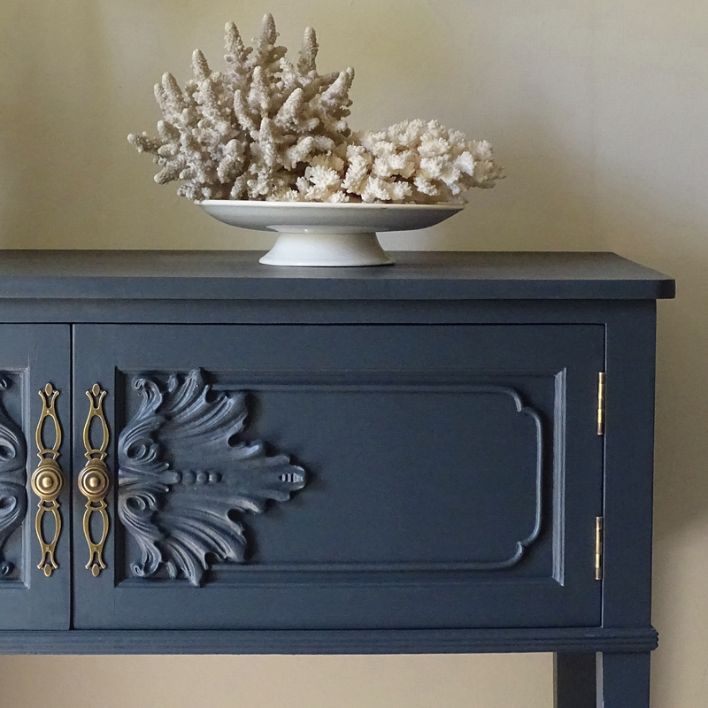 Decorative blue cabinet with ornate design and coral sculpture on top against a beige wall.