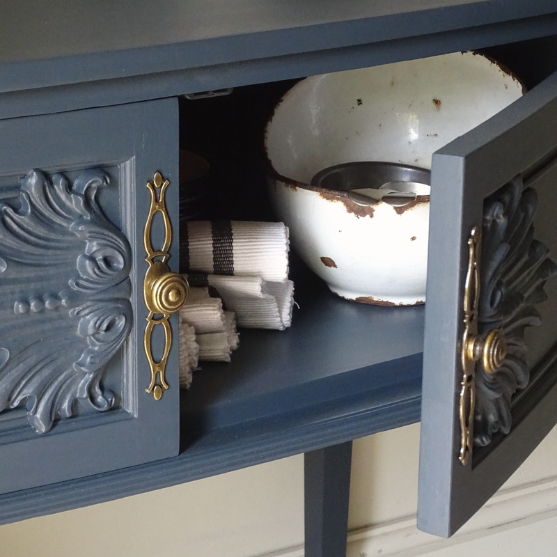 Decorative blue cabinet with open drawer containing a bowl and napkins.