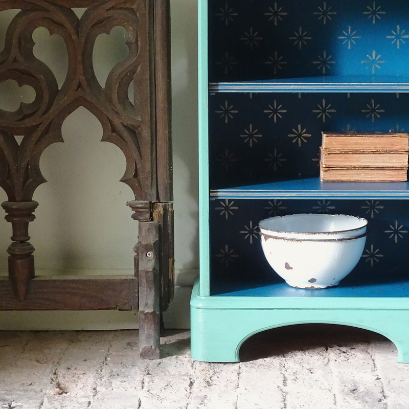 Verdigris cabinet with decorative interior, wooden ornament on left, and books on top.