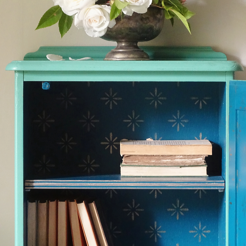 Verdigris cabinet with floral arrangement and books on a white background