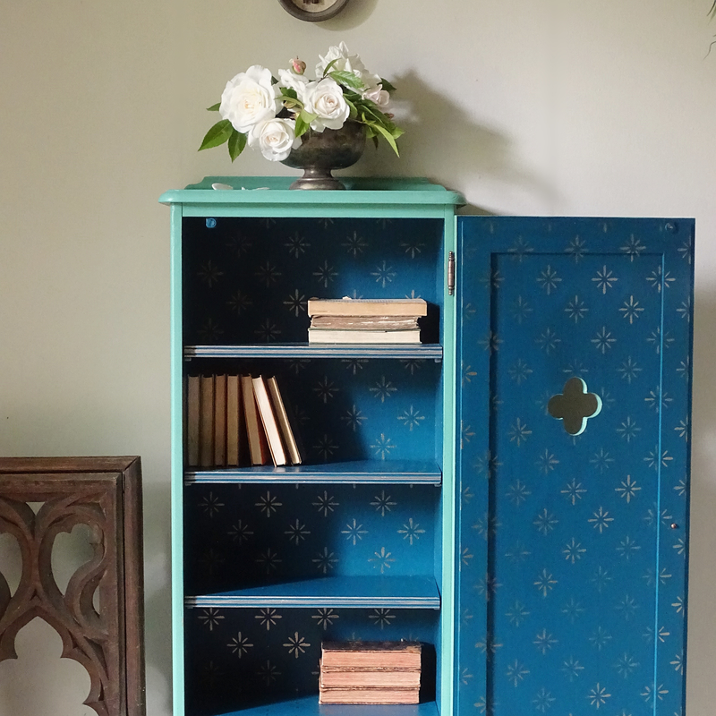 Verdigris cabinet with floral arrangement on top against a beige wall