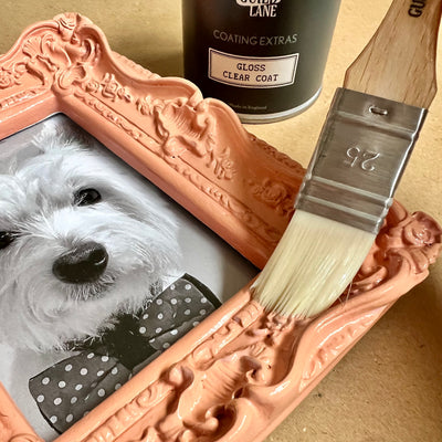 Decorative frame with a dog photo, paintbrush, and can of coating on a wooden surface