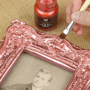 
                      
                        Decorative frame being gilded with a brush and rose gold paint.
                      
                    
