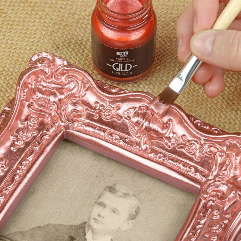 Decorative frame being gilded with a brush and rose gold paint.