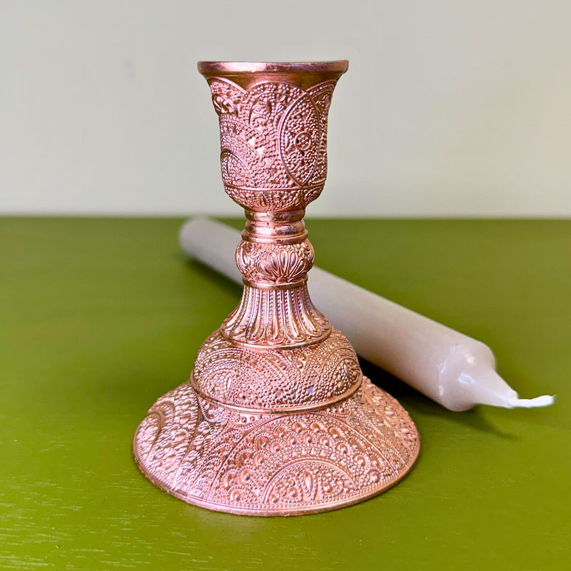 Decorative rose gold candle holder with a white candle on a green surface