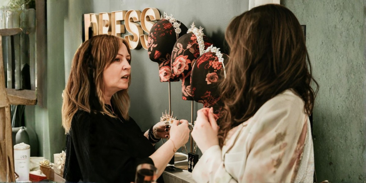 Two women in a hair salon with floral headbands on display.