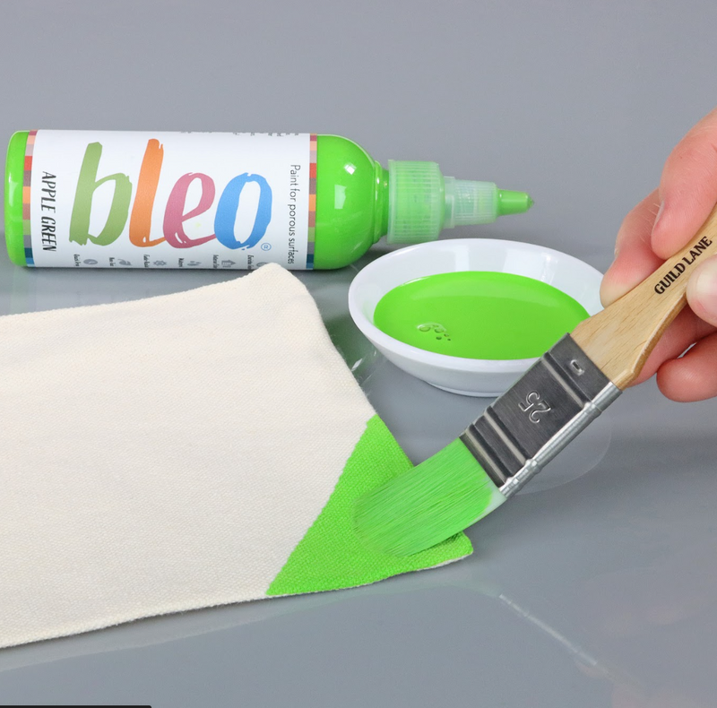 Person using a brush to apply green paint from a bottle labelled 'bleo' onto a white surface.