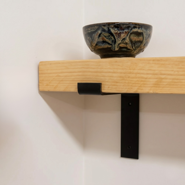 Ceramic bowl on a wooden shelf with a black bracket against a white wall
