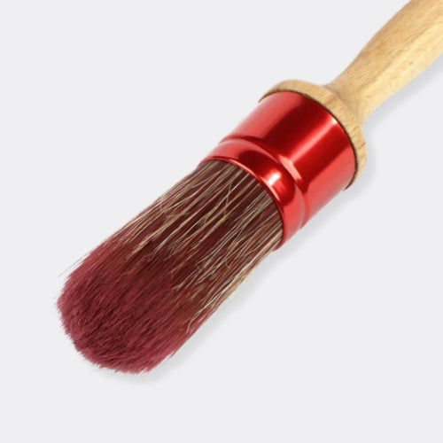 A close-up of a paint brush with reddish-brown bristles, a shiny red metal ferrule, and a light natural wood handle, shown on a light grey background.