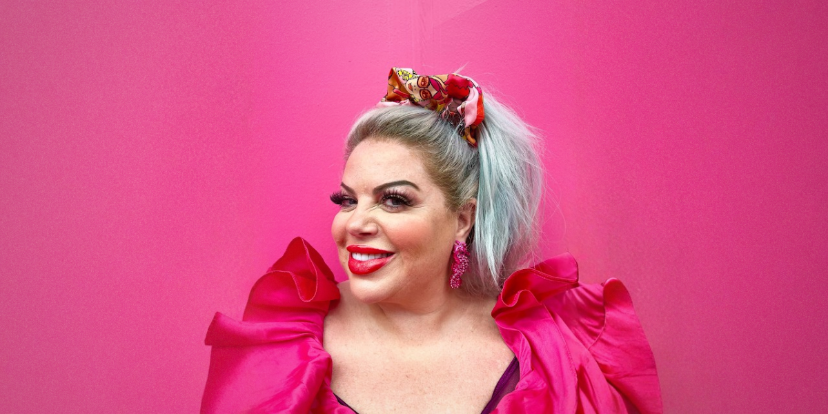 Person with colorful hair and clothing against a pink background