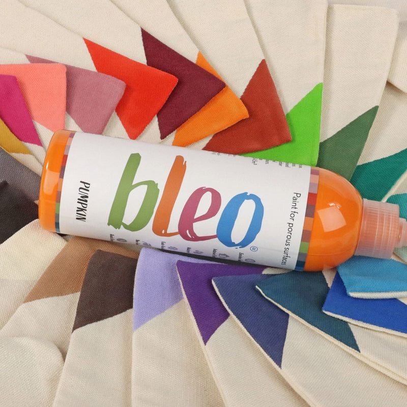 A bottle of Bleo laid diagonally across a fan of painted fabric swatches