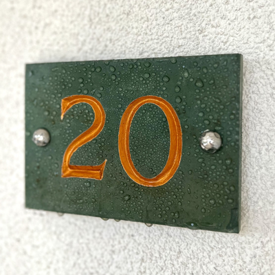 Green house number plate with '20' in orange on a textured white background