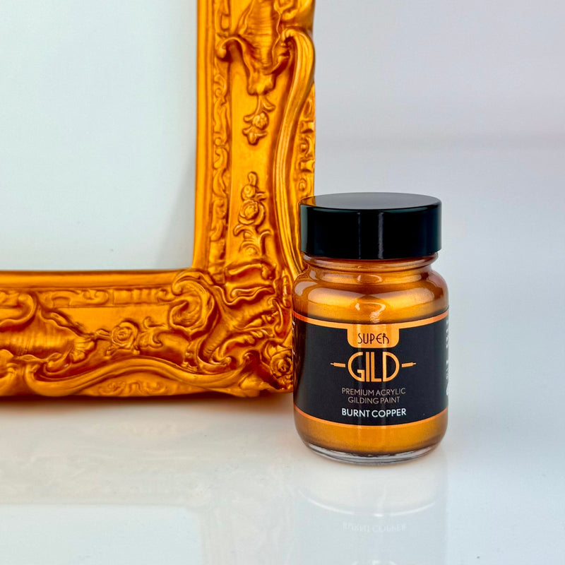 Jar of Super GILD Burnt Copper acrylic gilding paint next to a gold decorative frame on a white background