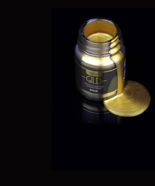 Bottle of gold acrylic paint with a small amount spilled on a black background