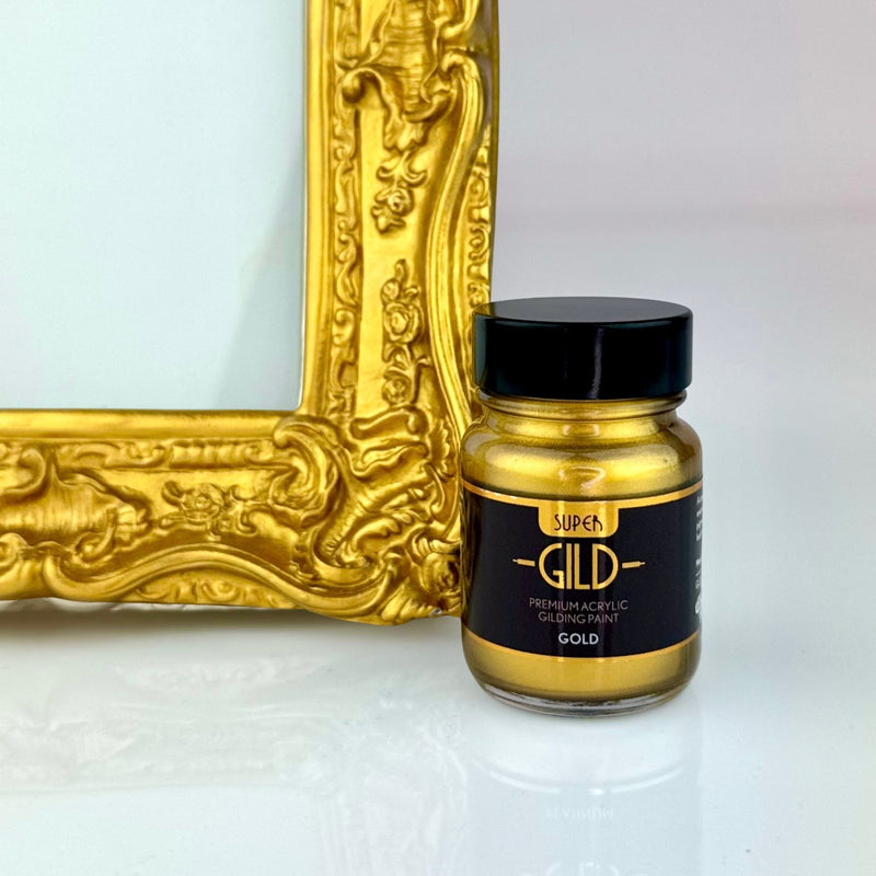 Jar of Super GILD gold acrylic gilding paint next to a gold decorative frame on a white background