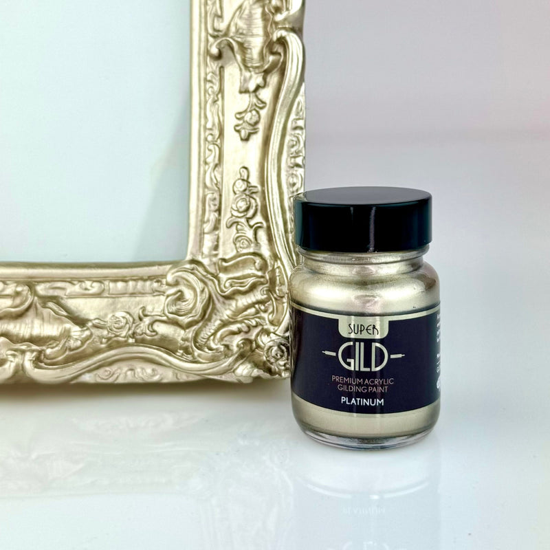 Jar of Super GILD Platinum acrylic gilding paint next to a gold decorative frame on a white background