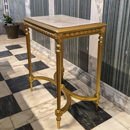 Gold-framed table with marble top in a room with checkered floor and marble walls.