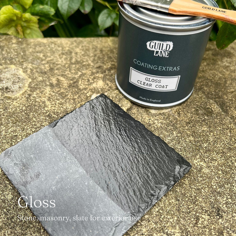 Can of Guild Lane paint with a brush and sample on a stone surface