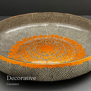 
                      
                        Decorative ceramic bowl with orange and black pattern on a dark background
                      
                    
