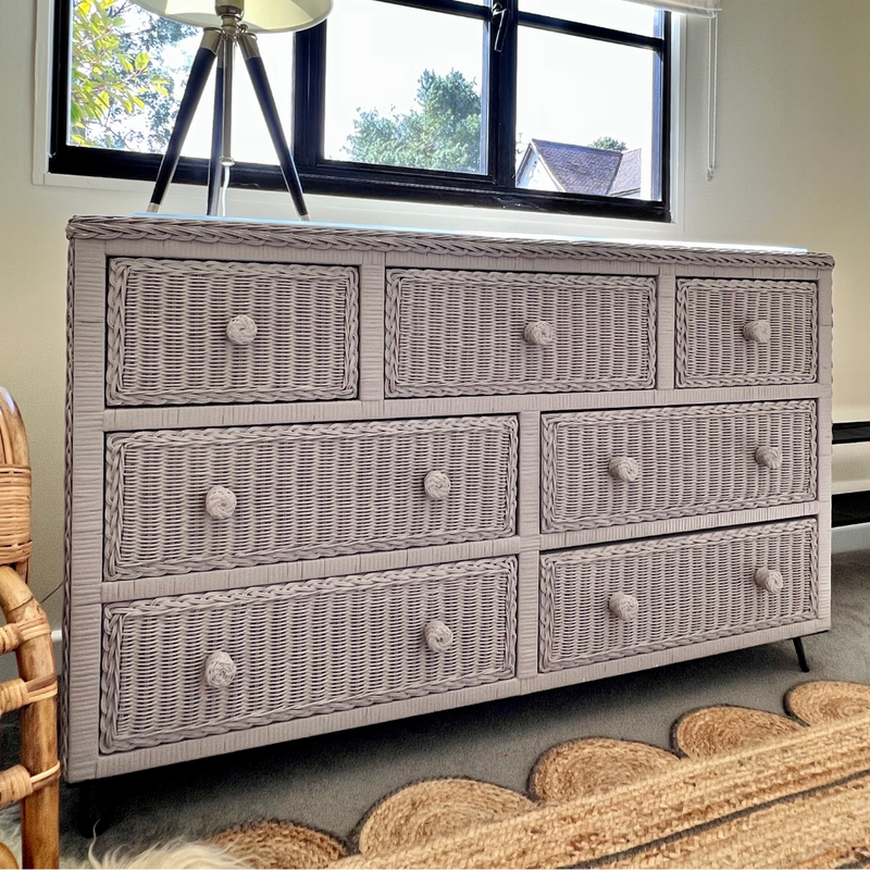 Painted Grey wicker dresser with multiple drawers in a room with a window and chair.