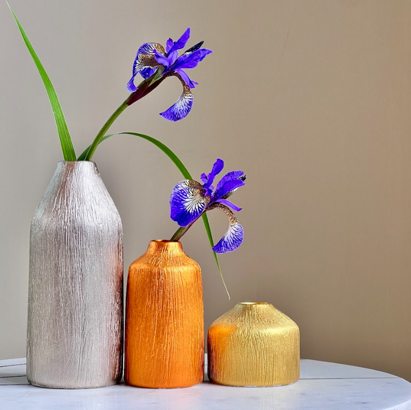 Three vases of different colors with a single purple flower on a neutral background
