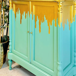 
                      
                        Green cabinet with gold accents and dripping paint effect
                      
                    