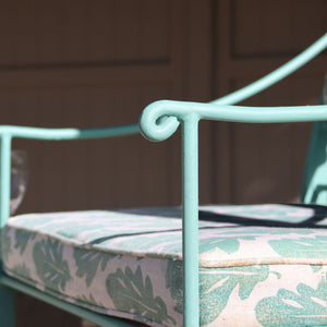 
                      
                        Verdigris metal chair with a cushion featuring leaf patterns on a blurred background
                      
                    