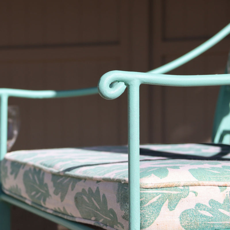 Verdigris metal chair with a cushion featuring leaf patterns on a blurred background