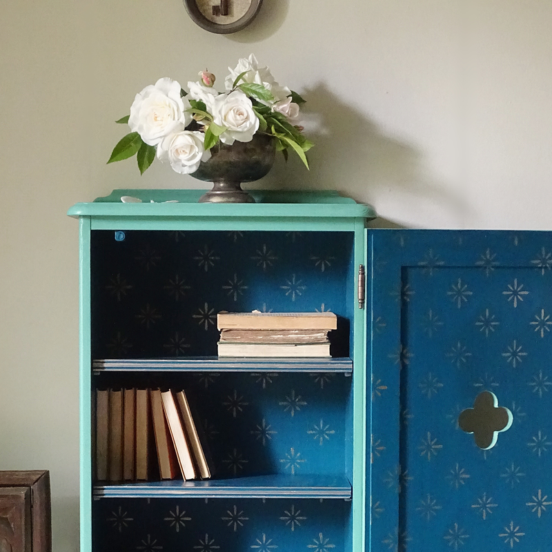 Verdigris cabinet with floral arrangement and books against a light wall