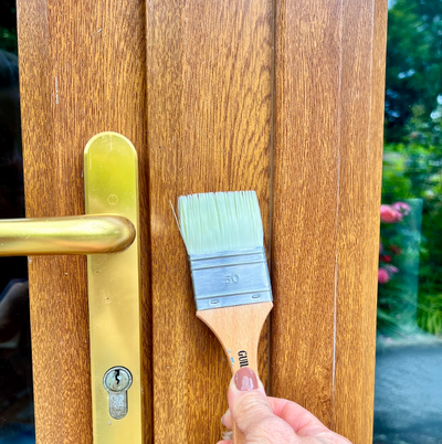 Person holding a paintbrush against a wooden door with a gold handle.