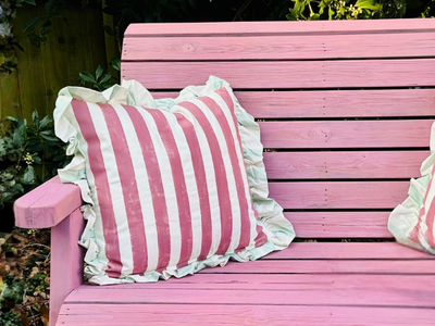 Pink wooden bench with a striped pillow on a blurred natural background