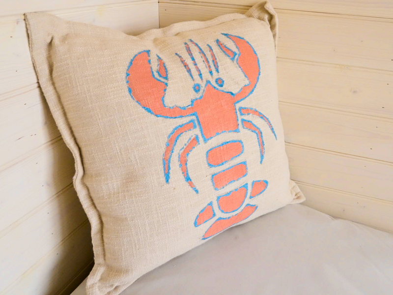 A linen cushion painted with an orange and blue lobster