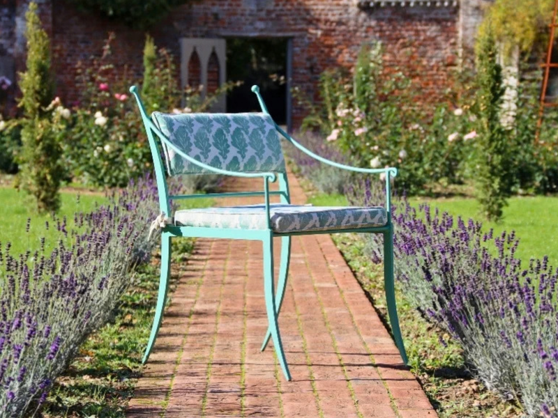 A metal garden bench painted pale green on a brick path between lavender