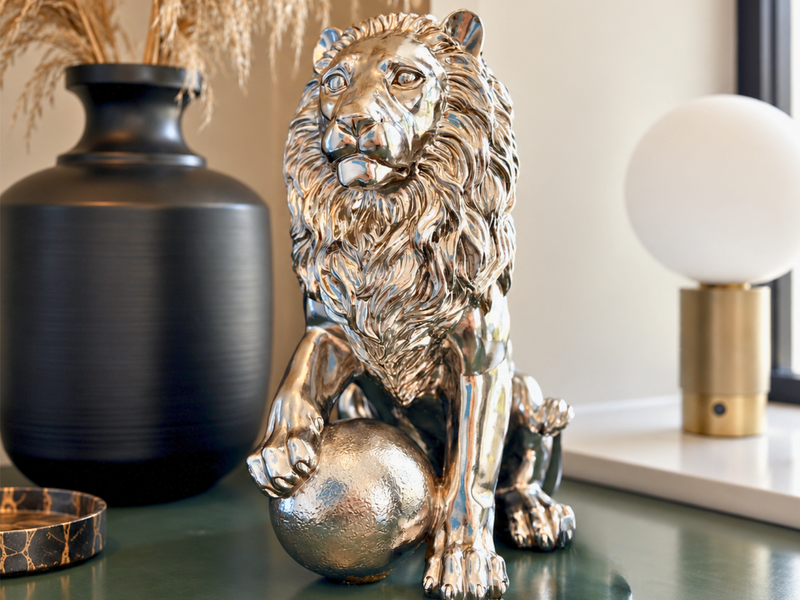 A lion ornament with a polished silver mirror finish, beside a black vase and a globe lamp