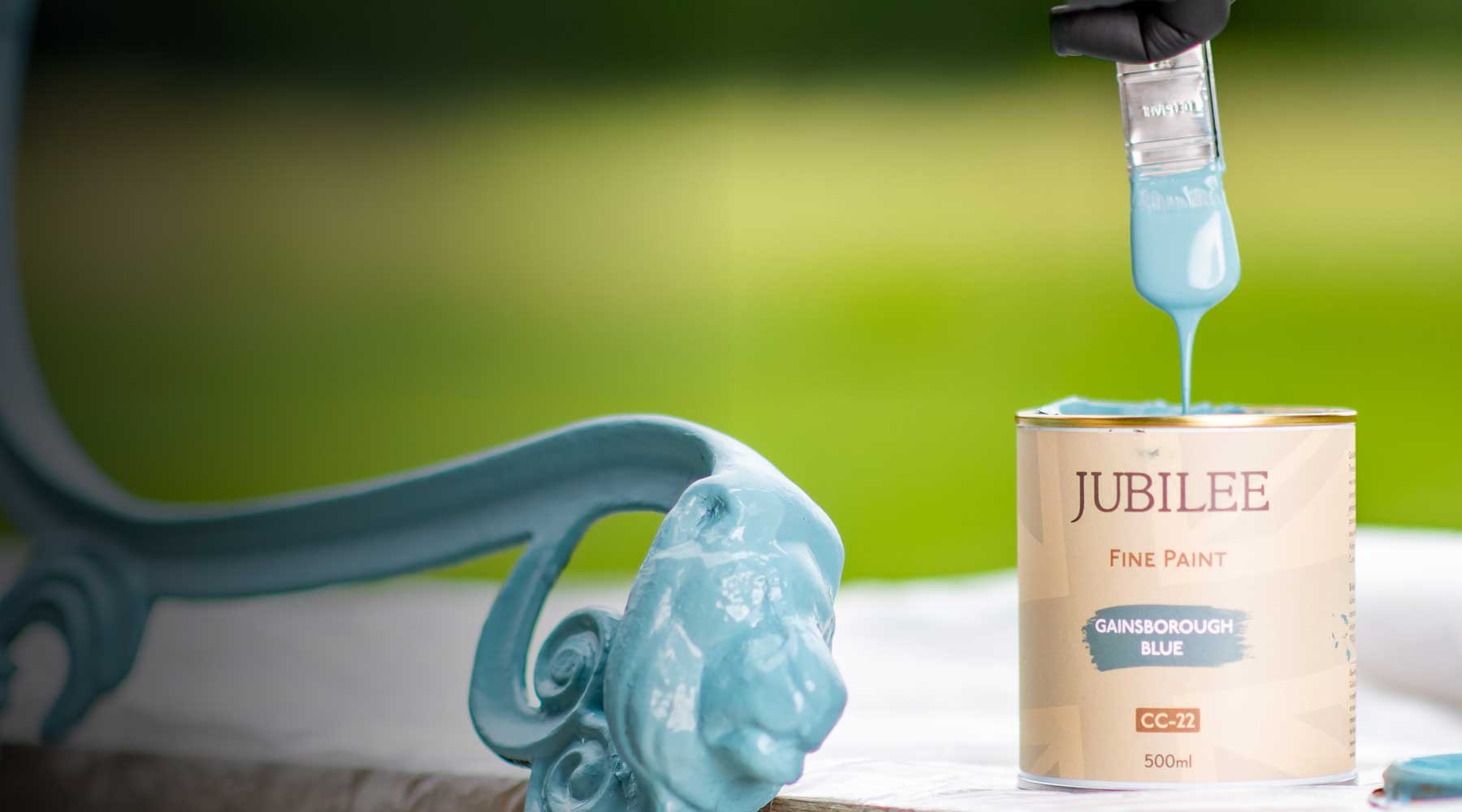 Jubilee Fine Paint can with blue paint being applied to a decorative object outdoors.