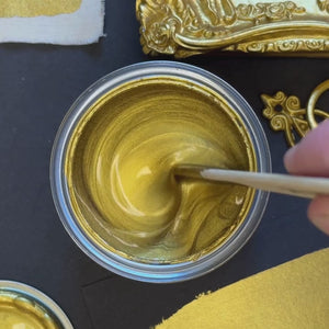 
                      
                        Load and play video in Gallery viewer, A hand stirs a classic, vivid yellow-gold metallic paint with a wooden stick. The video shows a brush applying a bold, opaque gold stroke onto a black surface, demonstrating the paint&amp;#39;s intense luminosity and &amp;quot;liquid gold&amp;quot; effect.
                      
                    