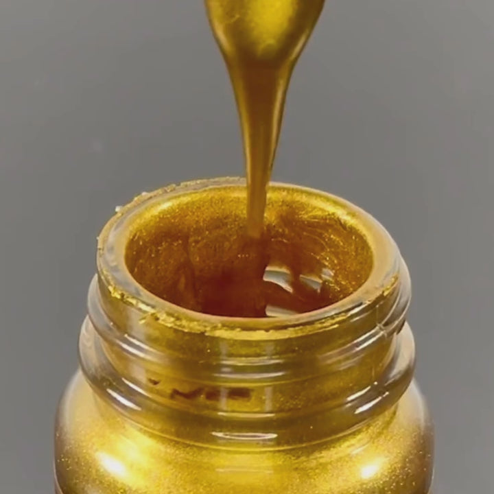 A close-up demonstration of three Super GILD premium acrylic metallic paints—Gold, Burnt Copper, and Platinum. The video shows the rich, thick consistency of the metallic pigment being stirred with a glass dropper, followed by the three labelled jars displayed on a reflective black surface.