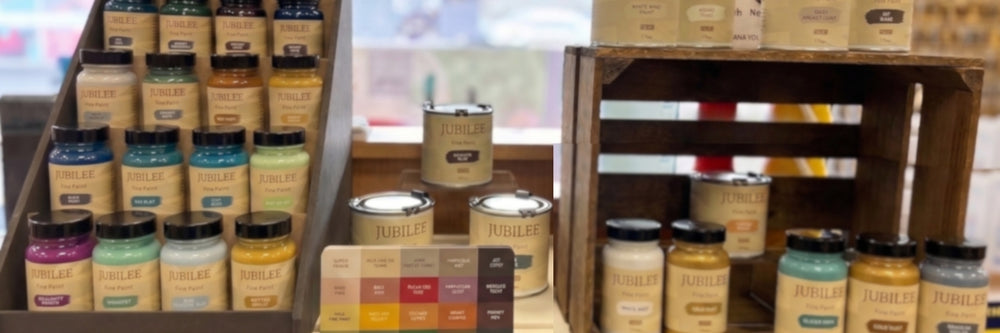 A display of Jubilee brand paint cans and jars arranged on wooden shelves and crates in a store or showroom setting.